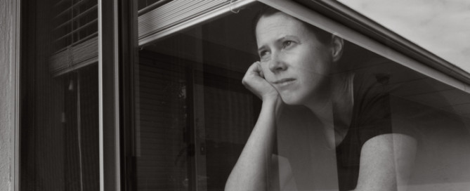 Sad adult woman (age 30-40) looking out through home window.