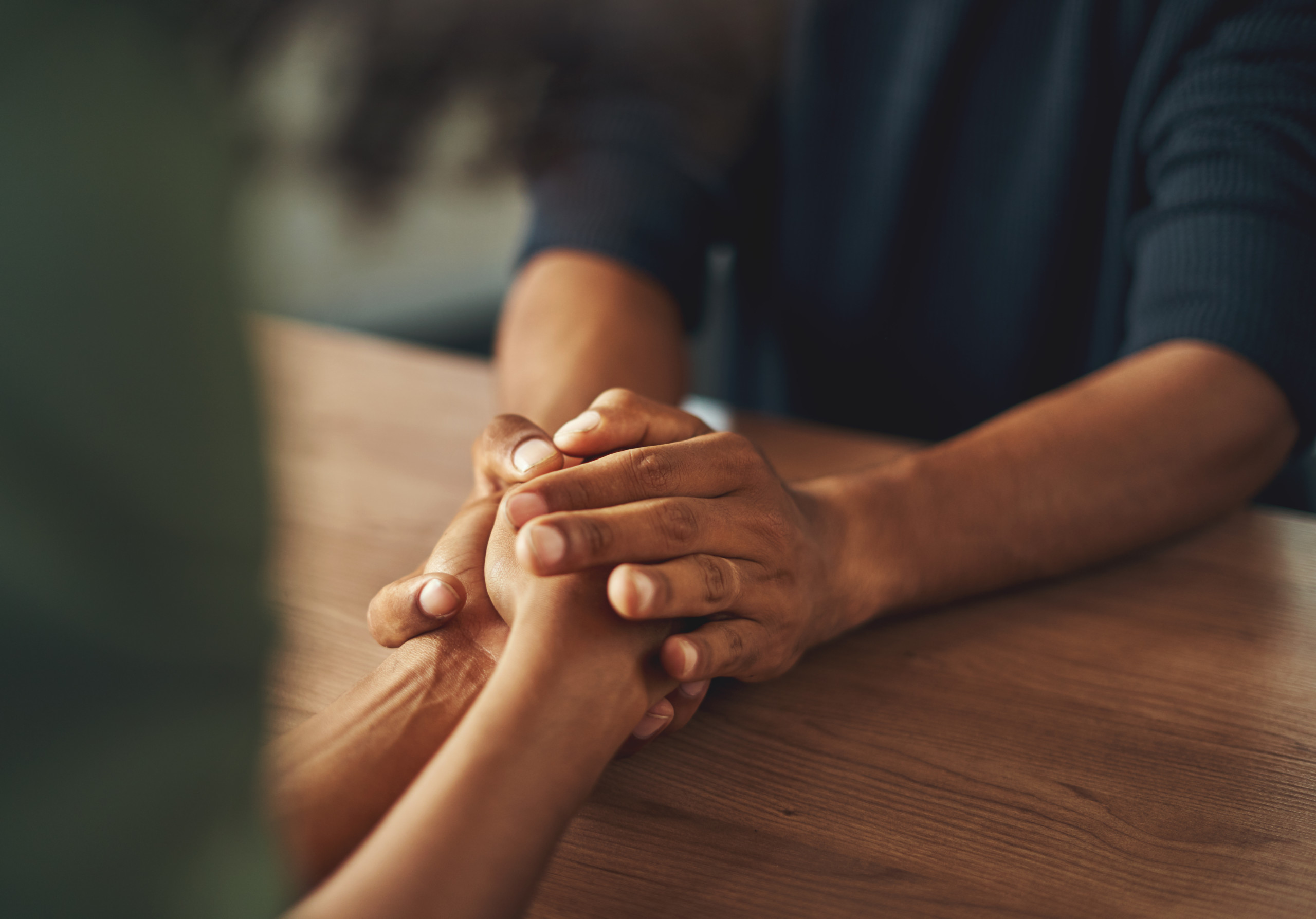 Close-up of man holding his girlfriend's hand over the wooden table
